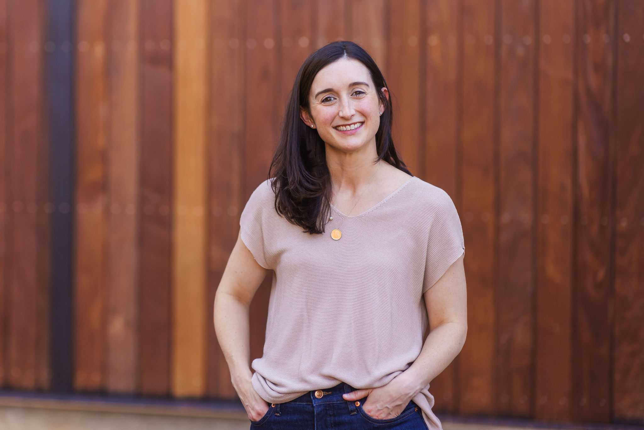 A woman in a pink shortsleeved shirt smiled at the camera. Wooden structure in background.